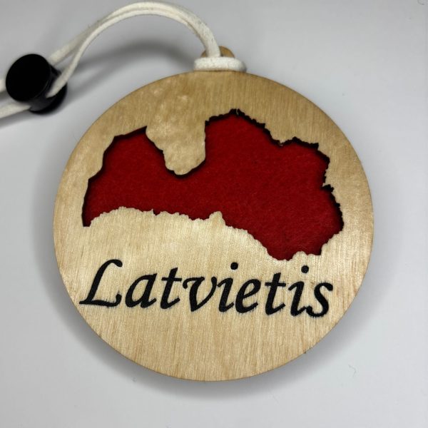 Karināms koka auto gaisa atsvaidzinātājs ar Latvijas kontūras izgriezumu, uzrakstu "Latviete" un sarkanu filca pamatni.