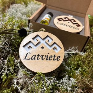 Karināms koka auto gaisa atsvaidzinātājs ar personalizētu gravējumu "Latviete" un baltu filca pamatni uz dabisku sūnu fona.